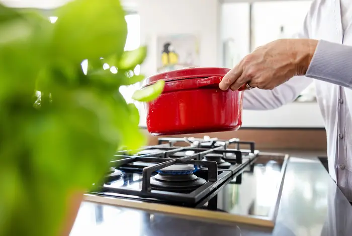Eine Hand setzt einen roten Topf auf einen Gasherd.