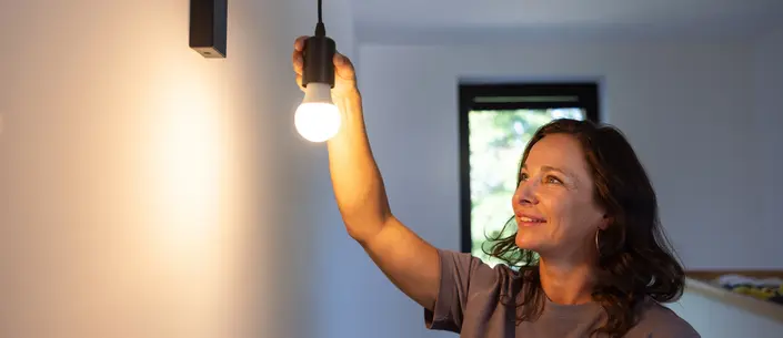 Frau, die eine Glühbirne in eine Deckenlampenfassung schraubt.