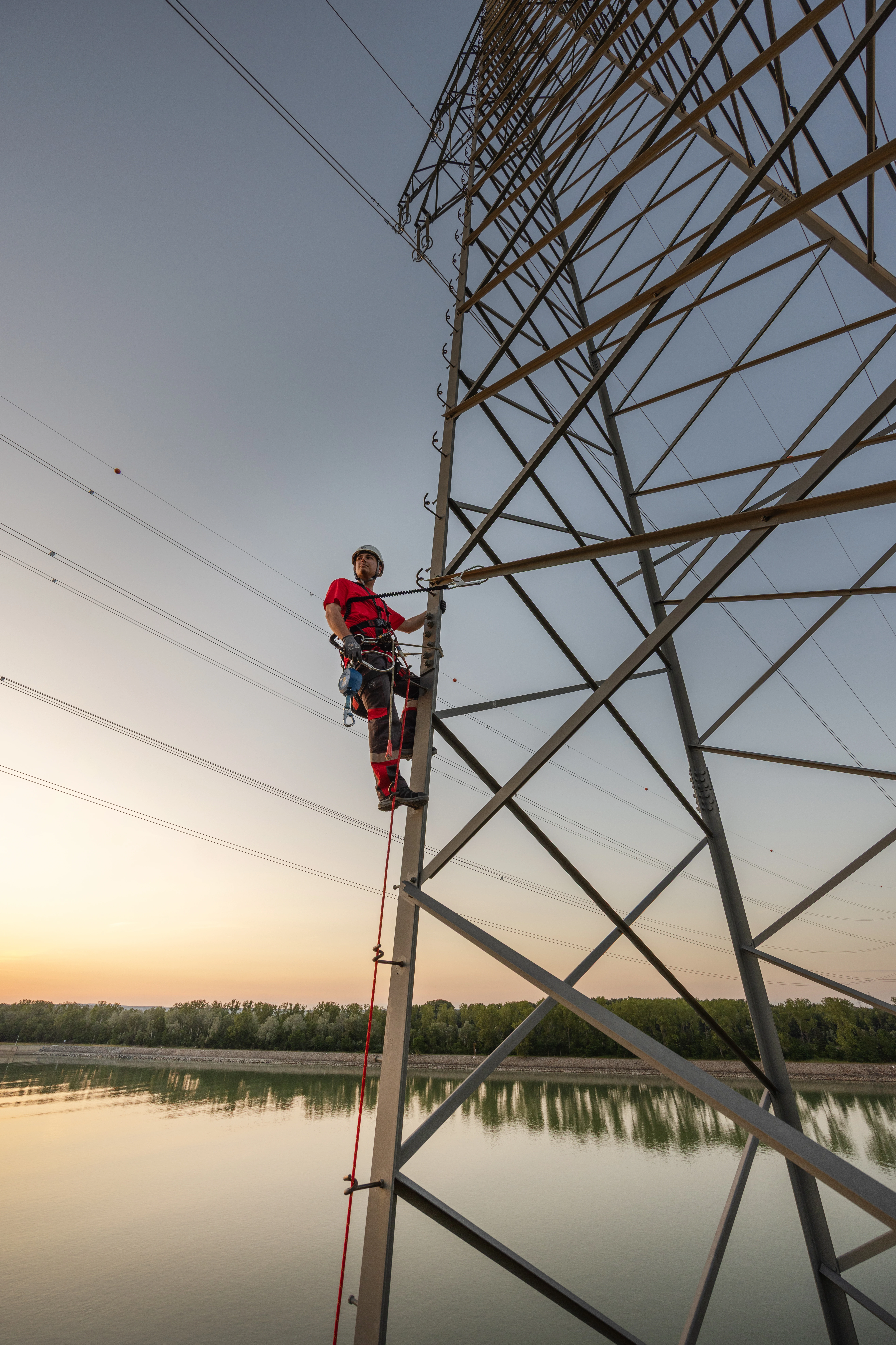 Netz NÖ Mitarbeiter klettert auf einen Strommast in der Dämmerung. Im Hintergrund die Donau.