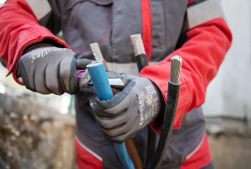 Hände eines Netz NÖ Monteur, der mit einer Zange an einem Kabel arbeitet.