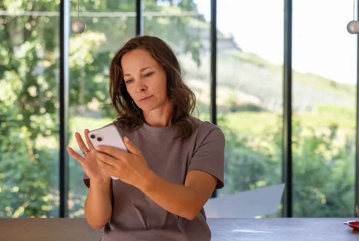 Frau steht an Kochzeile gelehnt mit Handy in der Hand.