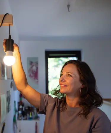 Frau, die eine Glühbirne in eine Deckenlampenfassung schraubt.