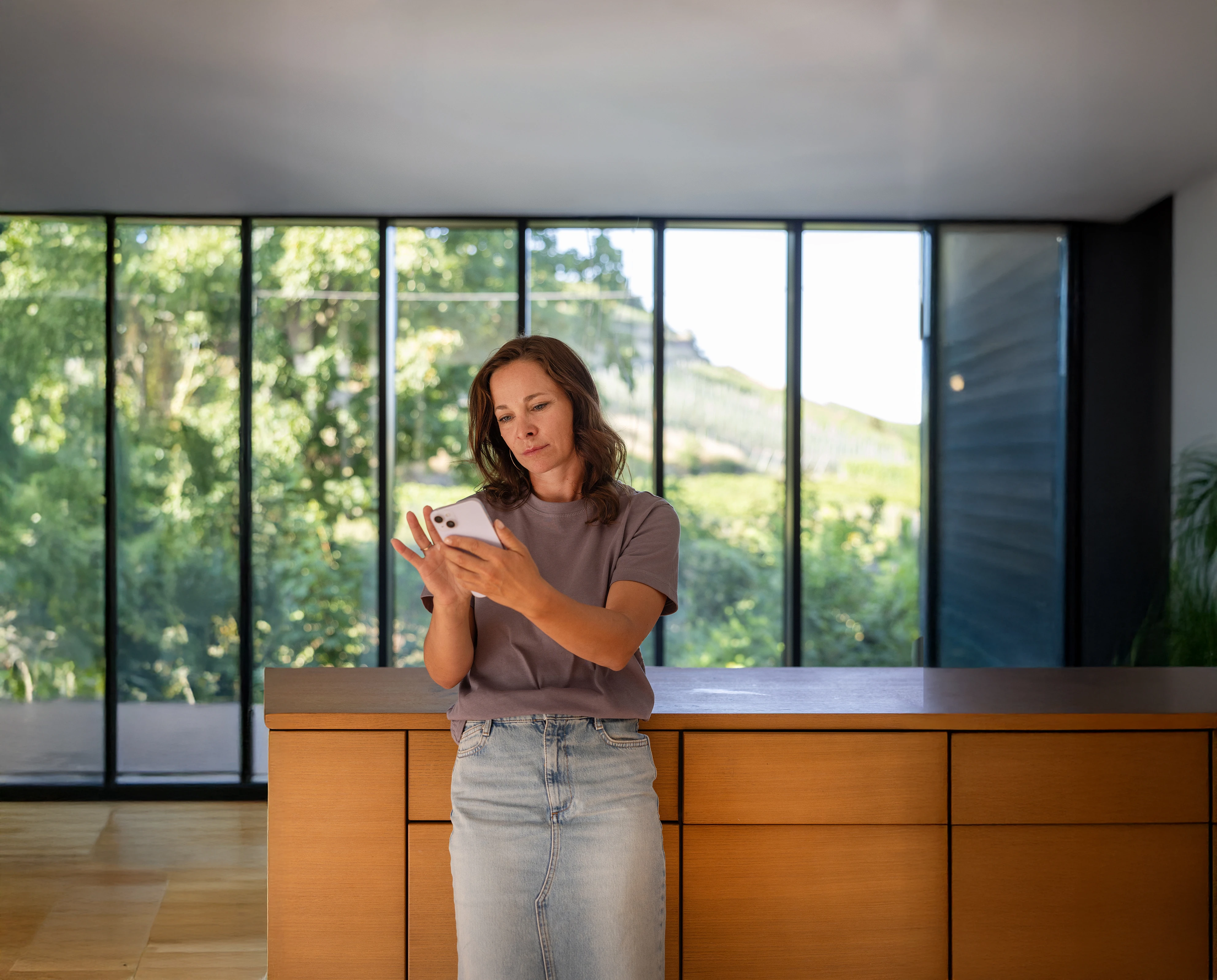 Frau steht in Wohnbereich und swiped auf ihrem Smartphone