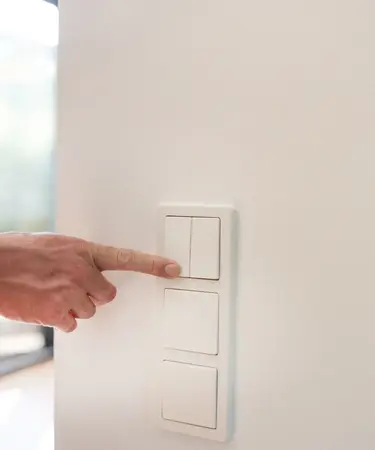Eine Männerhand aktiviert einen Lichtschalter an einer Wand.