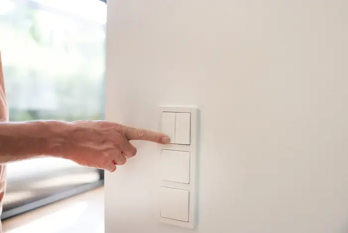 Eine Männerhand aktiviert einen Lichtschalter an einer Wand.