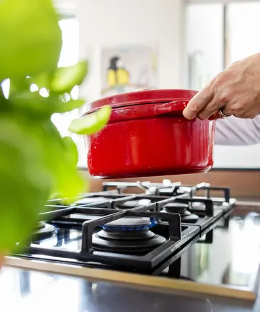 Eine Hand setzt einen roten Topf auf einen Gasherd.