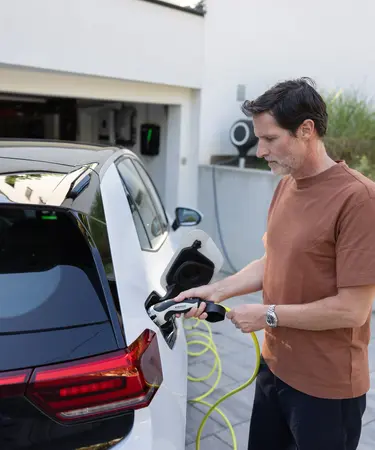 Mann lädt sein E-Auto vor seinem Haus.