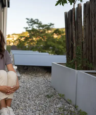 Frau sitzt auf Terrasse vor PV-Anlage.