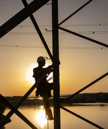Netz NÖ Mitarbeiter klettert auf Mast im Sonnenuntergang. Im Hintergrund die Donau.