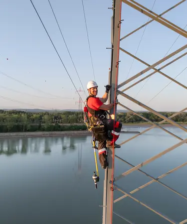 Netz NÖ Mitarbeiter mit Sicherheitskleidung auf Strommasten. Im Hintergrund die Donau.