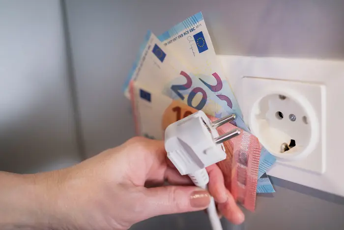 Hand hält Stromstecker und aufgefächerte Euroscheine vor einer Steckdose.