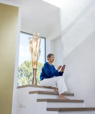 Ältere Frau sitzt auf Treppe mit Handy.