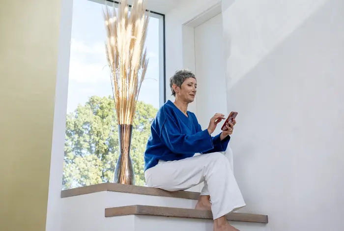 Ältere Frau sitzt auf Treppe mit Handy.