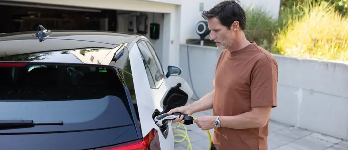 Mann lädt sein E-Auto vor seinem Haus.