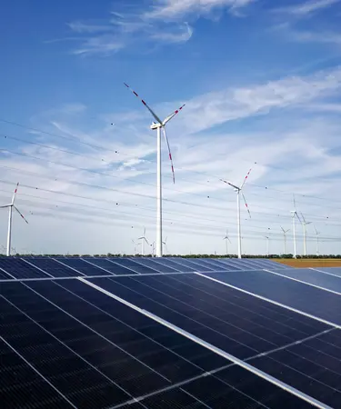 Im Vordergrund liegt eine Flächen PV-Anlage vor Windrädern. Im Hintergrund eine Stromleitung.