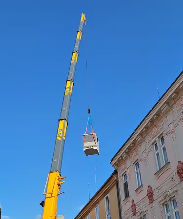 Eine neue Trafostation wird mittels Kran über ein Wohnhaus gehoben