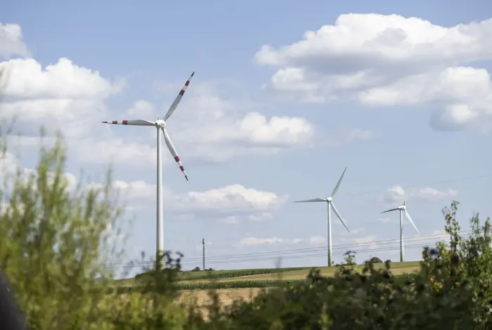 Windrad in frühsommerlicher Agrarlandschaft mit Stromleitung.