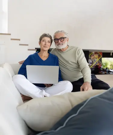 Älteres Pärchen auf Couch mit Laptop im Wohnzimmer