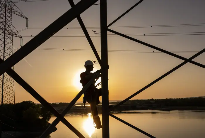 Netz NÖ Mitarbeiter klettert auf Mast im Sonnenuntergang. Im Hintergrund die Donau.