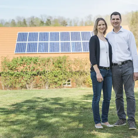 Paar auf Wiese, im Hintergrund Hausdach mit PV-Anlage