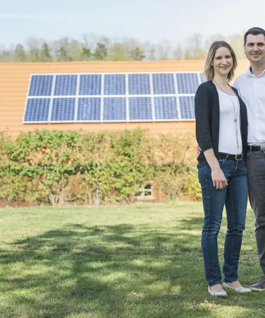 Paar auf Wiese, im Hintergrund Hausdach mit PV-Anlage