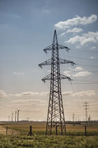 Hochspannungsmasten vor Dämmerstimmung. Im Hintergrund stehen Windräder.